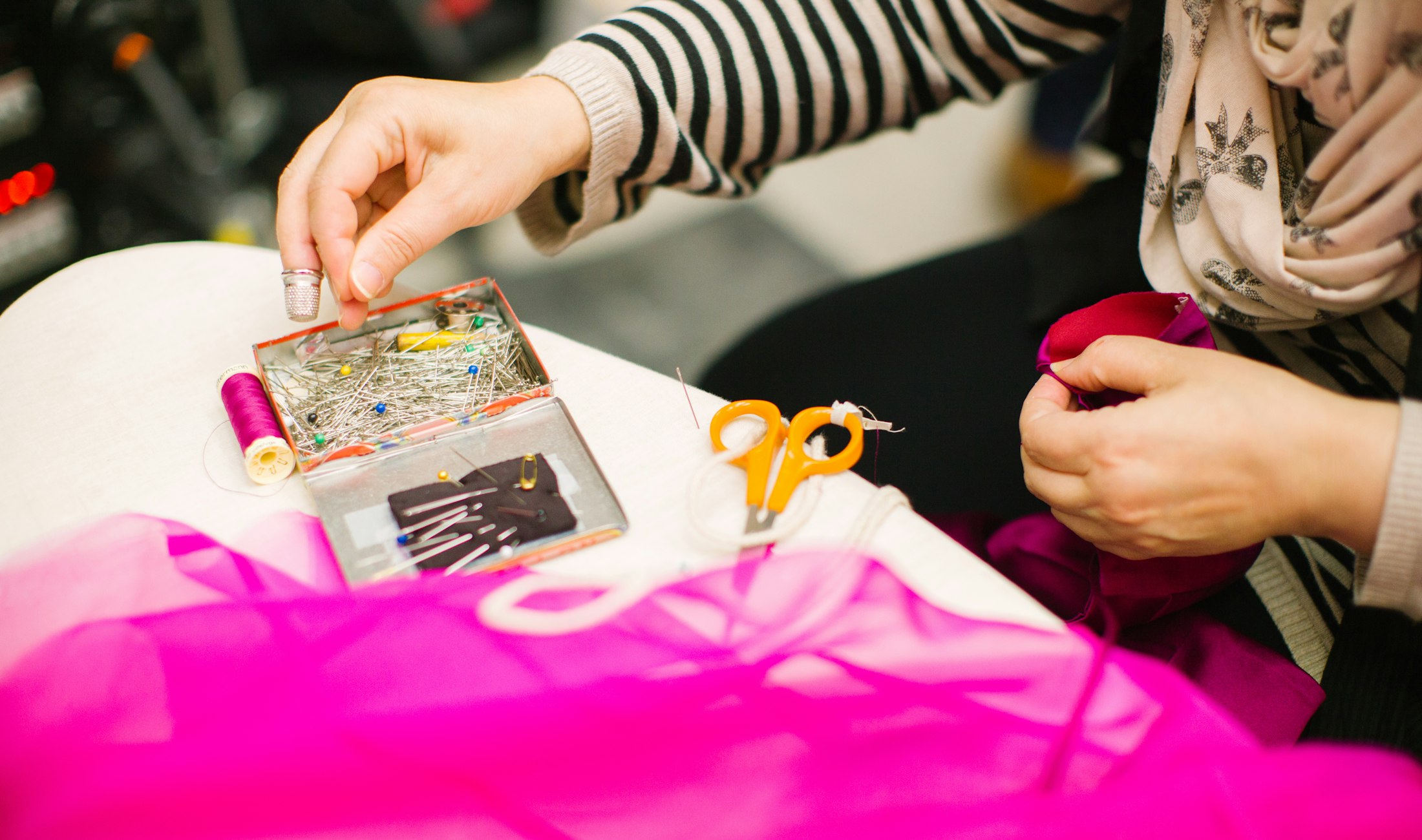 Mains préparant fil et épingles sur un tissu rose